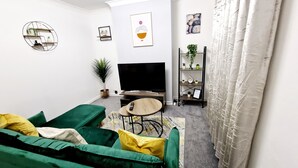 Un salon avec un canapé vert, une petite table ronde, un téléviseur et une plante.
