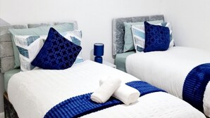 Deux lits jumeaux avec une literie blanche et bleue, une lampe bleue et une tête de lit grise.