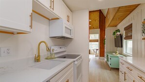 A modern kitchen with white cabinetry, a stainless steel sink, and a gold faucet. - Hope House- Vacation Village 1 Bedroom with Loft (Clermont)