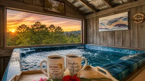 A hot tub with two mugs, a wooden tray with flowers, and a scenic sunset view. - Country Cabin• Fence Area for Dogs• Hot Tub• Games (Kodak)