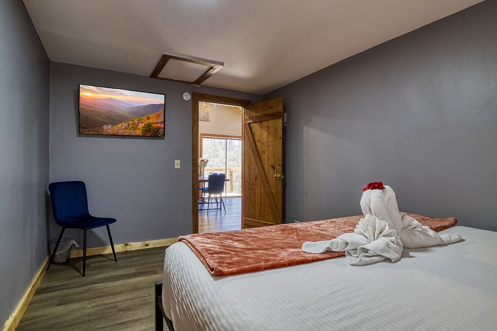 A hotel room with a bed, a chair, a painting, and a wooden door leading to an outdoor area.