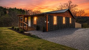 A two-story log cabin with a porch, a front door, and a gravel driveway.