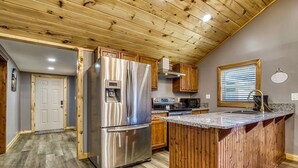 A modern kitchen with a stainless steel refrigerator, wooden cabinets, and a granite countertop island.