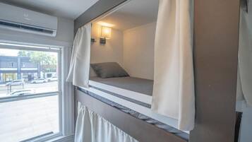 A bunk bed room with a window, air conditioning unit, and a wall-mounted light.