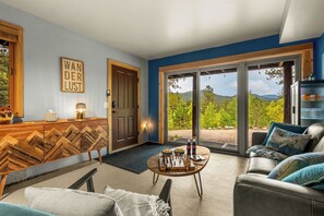 A spacious living area with a large sliding glass door leading to a scenic outdoor view, a wooden cabinet with a chessboard, and a cozy seating arrangement.