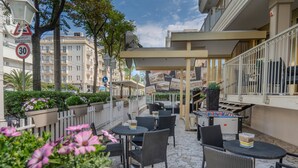 Un espace extérieur aménagé en terrasse, avec des tables et des chaises, une table de baby-foot et une clôture blanche.
