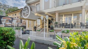 L’entrée d’un hôtel, avec une enseigne, des tables à l’extérieur et une clôture blanche.