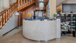 Un espace d’accueil d’hôtel avec un comptoir incurvé, un escalier en bois et un coin bar où sont exposées des bouteilles de vin.