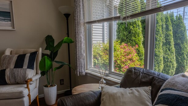 A cozy living room with a view of a garden through a large window, a potted plant, and a lamp. - Modern River Retreat Near Airport, Hospitals, Corporations (Wyandotte)