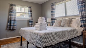 A bedroom with a bed, a stack of towels, and plaid curtains. - Modern River Retreat Near Airport, Hospitals, Corporations (Wyandotte)