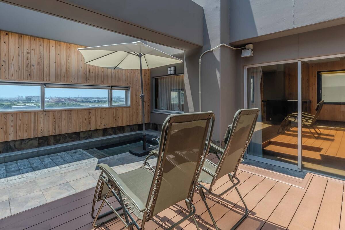 A modern outdoor deck with a view of the city, wooden paneling, and a glass door leading to another area.