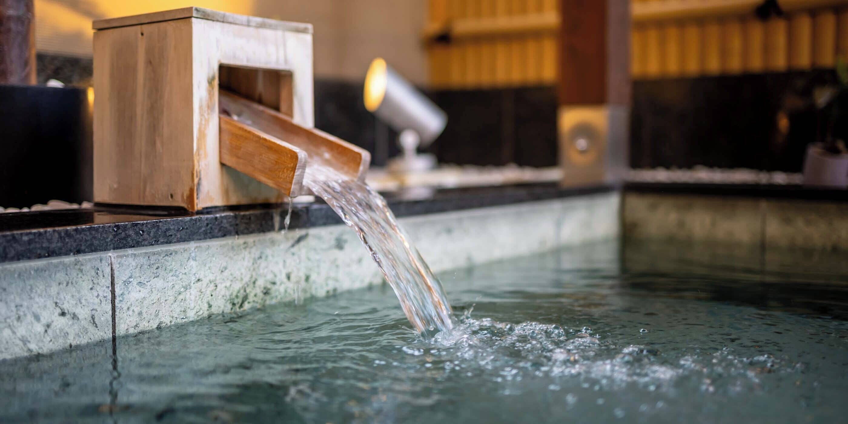 Una fuente de madera con agua que fluye hacia una piscina.