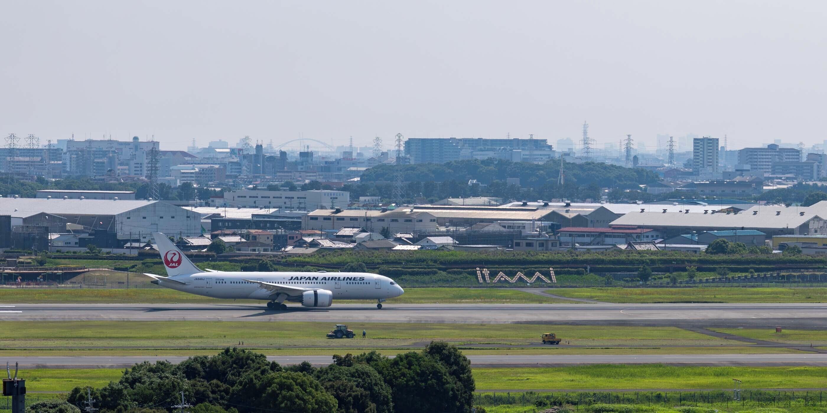 A Japan Airlines airplane on the runway with buildings and a cityscape in the background.