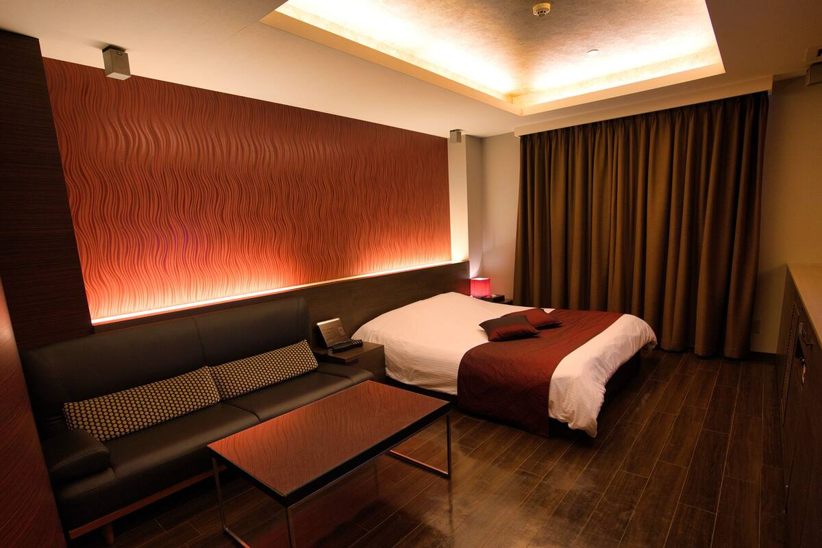 A modern hotel room with a bed, a sofa, a small table, and a wall with a wavy pattern.