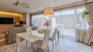 A modern living room with a TV, sofa, dining table, and large windows with sheer curtains. - HOTEL felice Osaka Itami airport (Toyonaka)