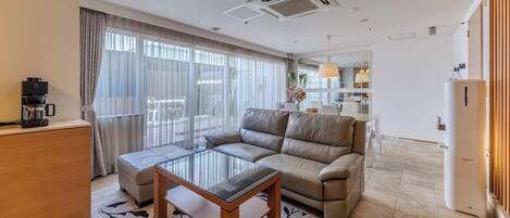 Una sala de estar moderna con una mesa de centro de vidrio, sofá de cuero y una zona de comedor con una mesa y sillas blancas.