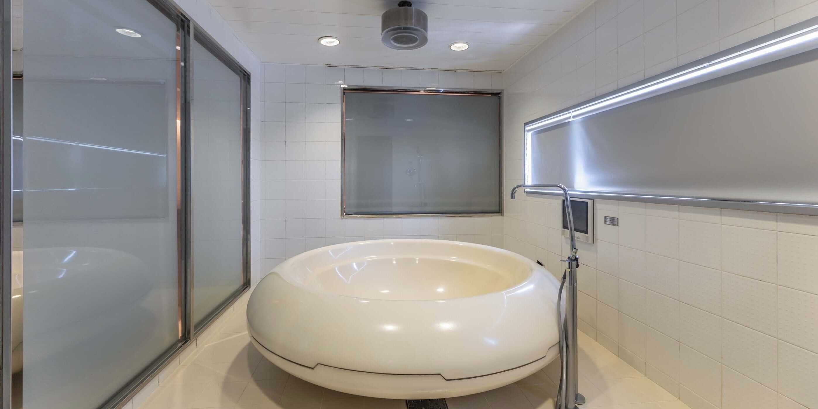 Un baño moderno con una bañera blanca grande y redonda, cabina de ducha de vidrio y barandilla de metal.