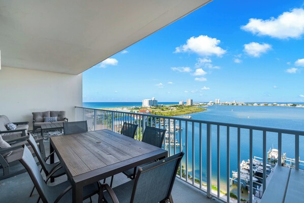 A balcony with a wooden table and chairs, overlooking a marina and a clear blue sky.