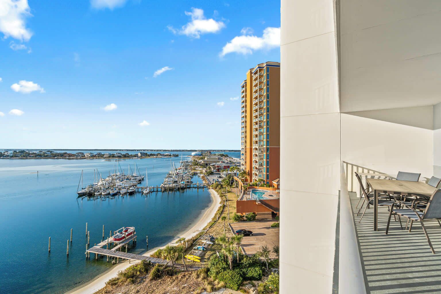 A coastal view with a marina, a tall hotel building, and a balcony with outdoor furniture.