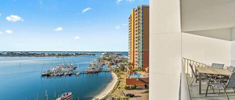 A coastal view with a marina, a tall hotel building, and a balcony with outdoor furniture.
