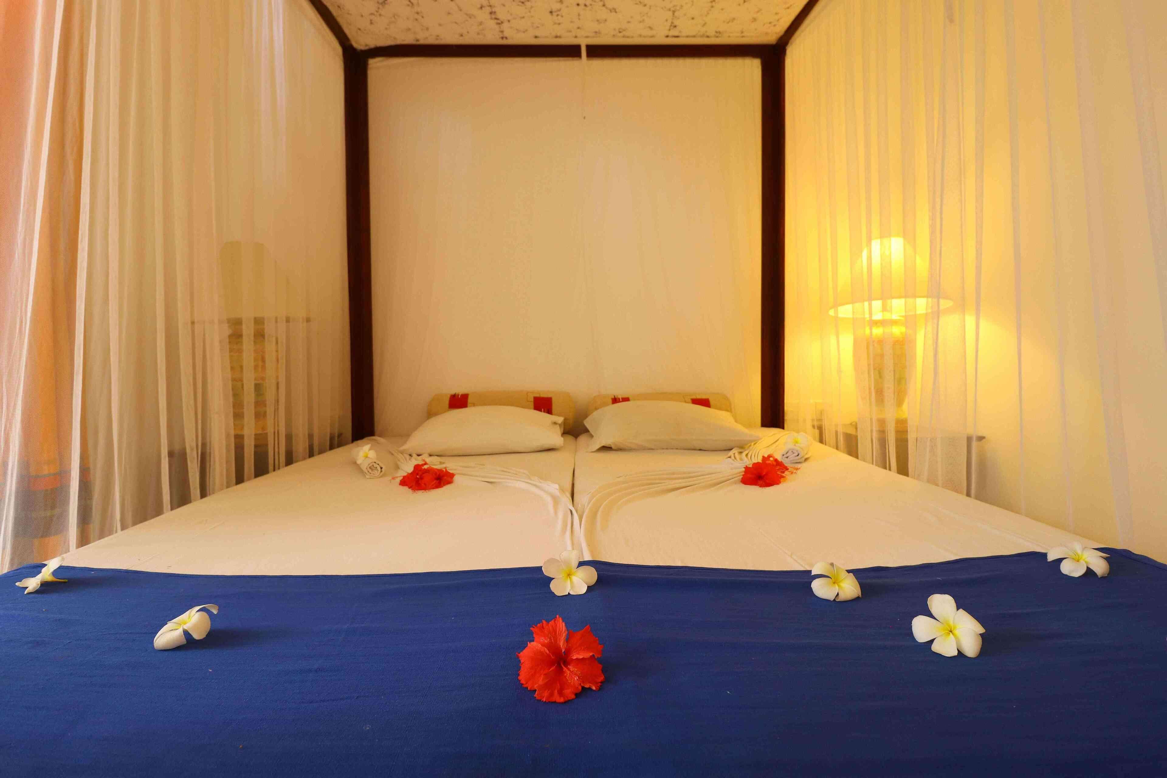 A double bed with white and red pillows, a blue bedspread, and white and red flowers.