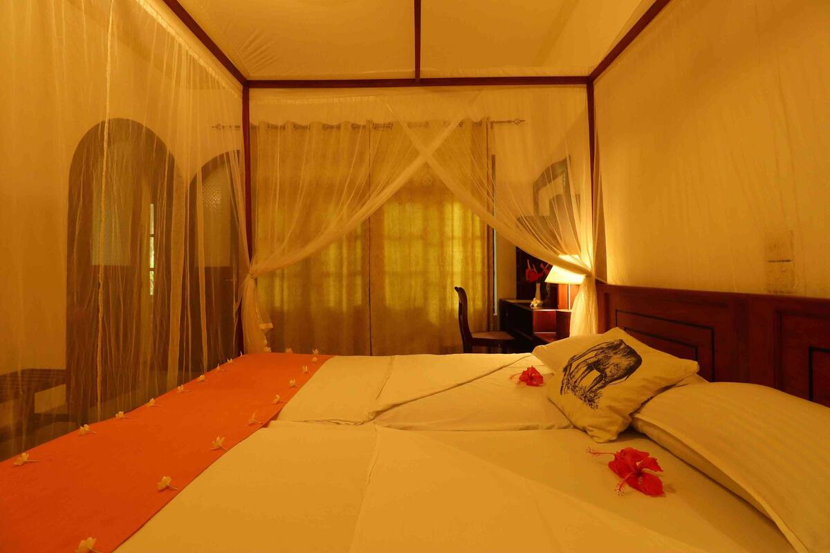 Een hotelkamer met een bed, nachtkastje, lamp en een raam met gordijnen.