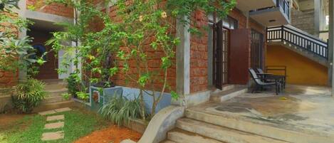A multi-level building with a brick facade, a staircase leading to a balcony, and a small garden area with steps and potted plants.