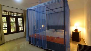 A room with a bed under a mosquito net, a nightstand with a lamp, and a window with curtains.