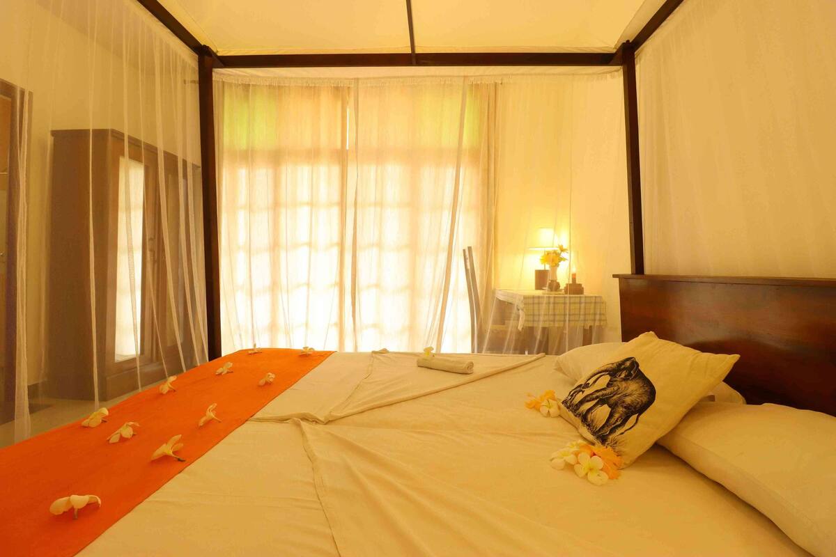 Een hotelkamer met een bed, een nachtkastje met een lamp en dunne gordijnen.