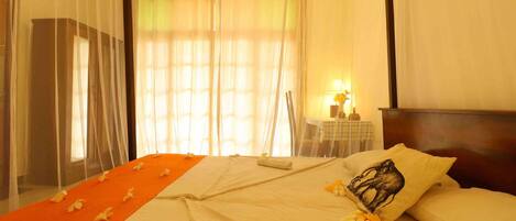 Una habitación de hotel con una cama, una mesita de noche con lámpara y cortinas translúcidas.