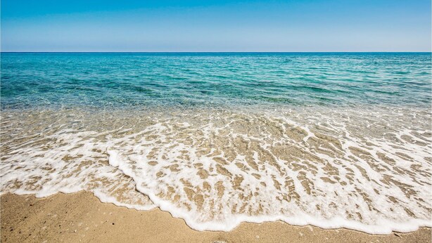 Une plage avec une eau cristalline, un rivage sablonneux et un ciel dégagé.
