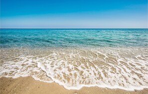 A beach with clear water, sandy shore, and a clear sky.