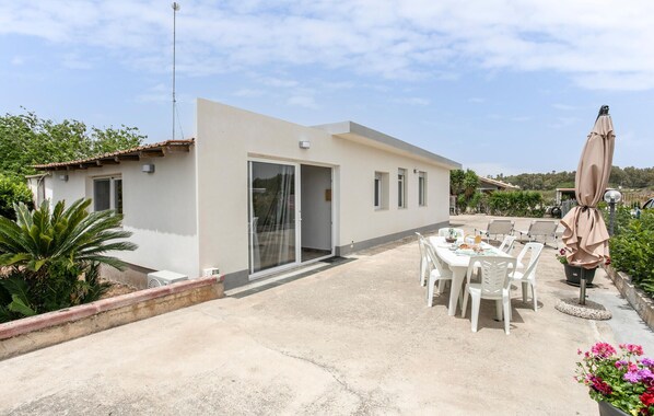 Une maison moderne dotée d’un patio, d’un coin repas avec des chaises et d’un espace extérieur aménagé et couvert.