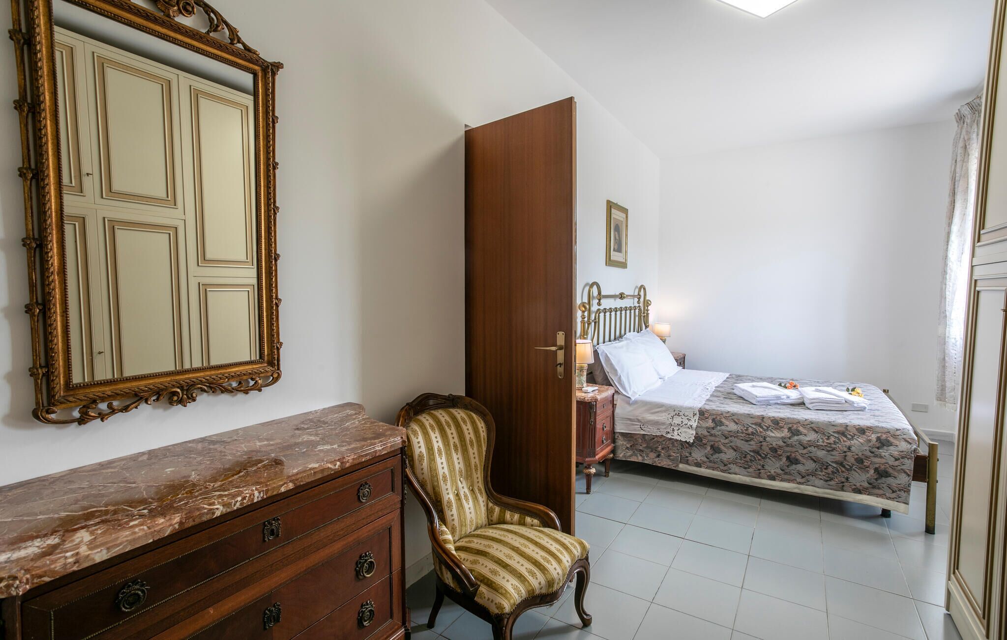 Ein Schlafzimmer mit Bett, Stuhl, Kommode, Spiegel und einer Tür.