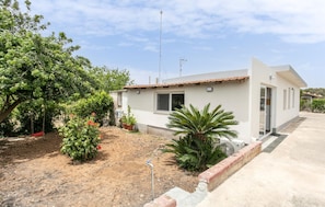 A single-story house with a white exterior, a tiled roof, and a small garden with various plants and a swing. - Amazing home in Santa Maria del Focall (Santa Maria del Focall)