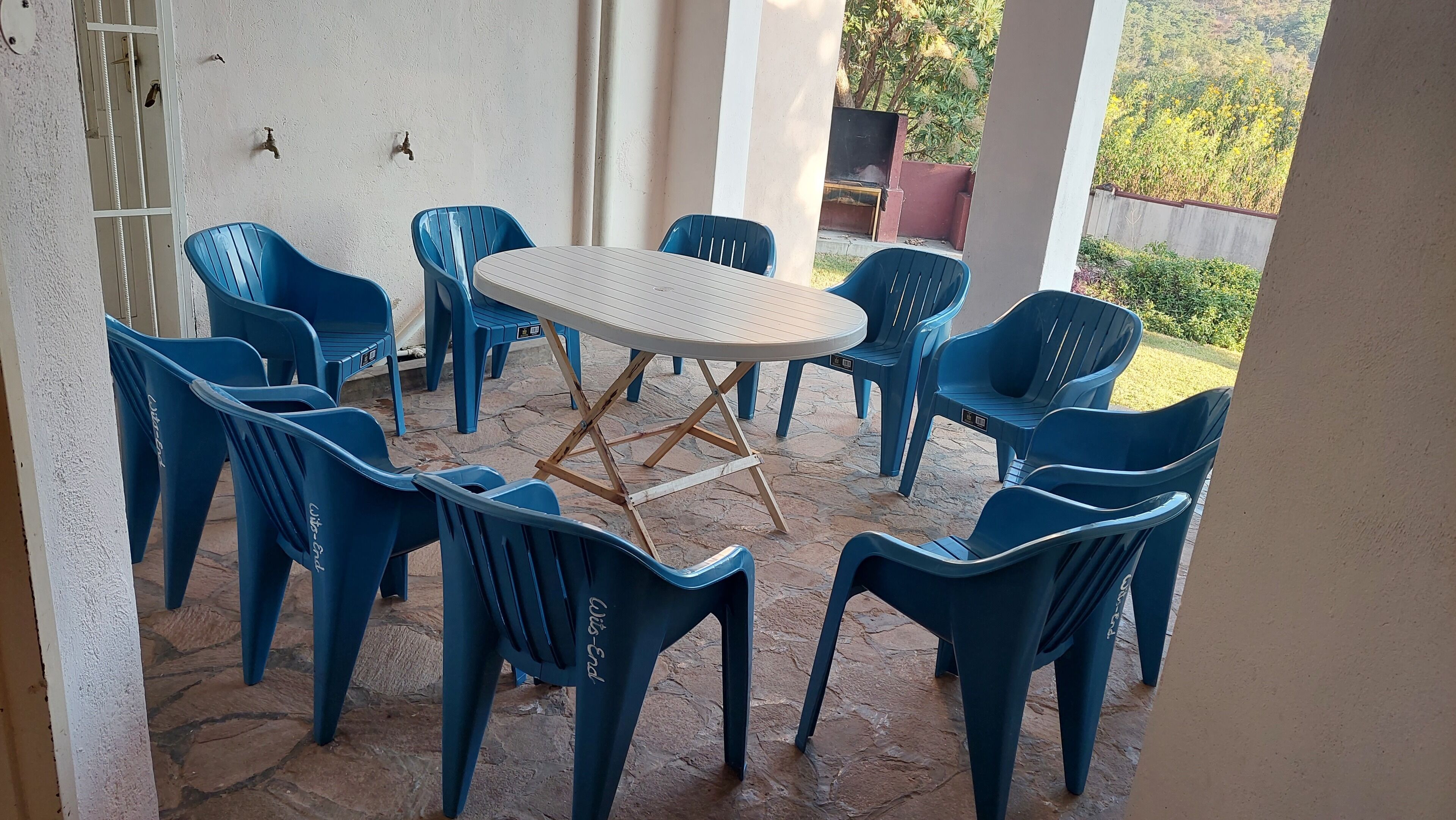 Un'area salotto esterna coperta con un tavolo rotondo e sedie di plastica blu.