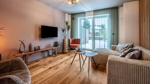 A modern living room with a flat-screen TV, wooden flooring, a sofa, a small table, and a bench.