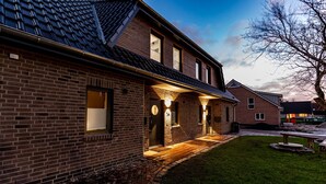 A brick house with a tiled roof, a front porch, and a small lawn area.