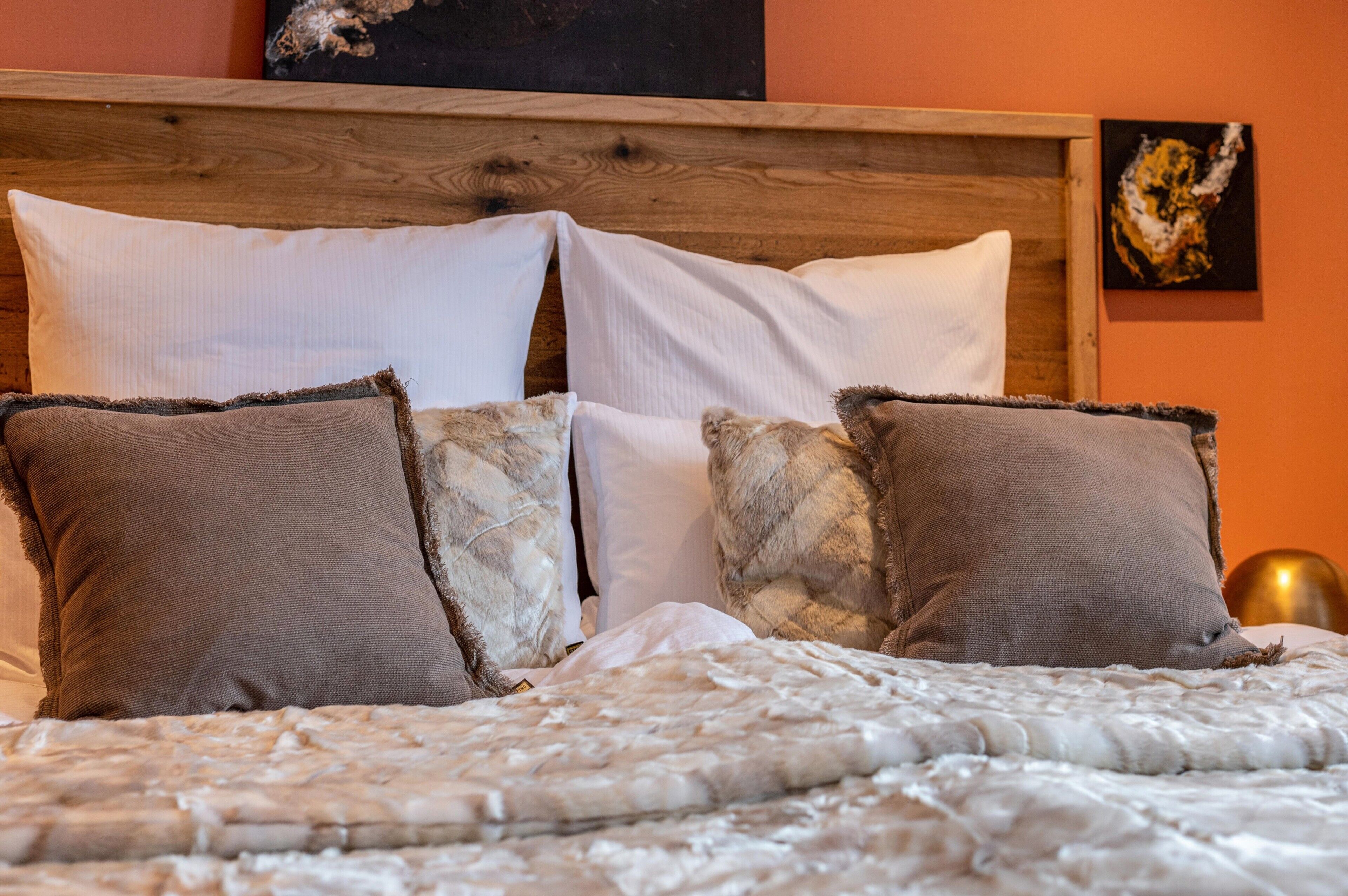 Un letto con una testiera in legno, cuscini bianchi e marroni e una coperta con trama.