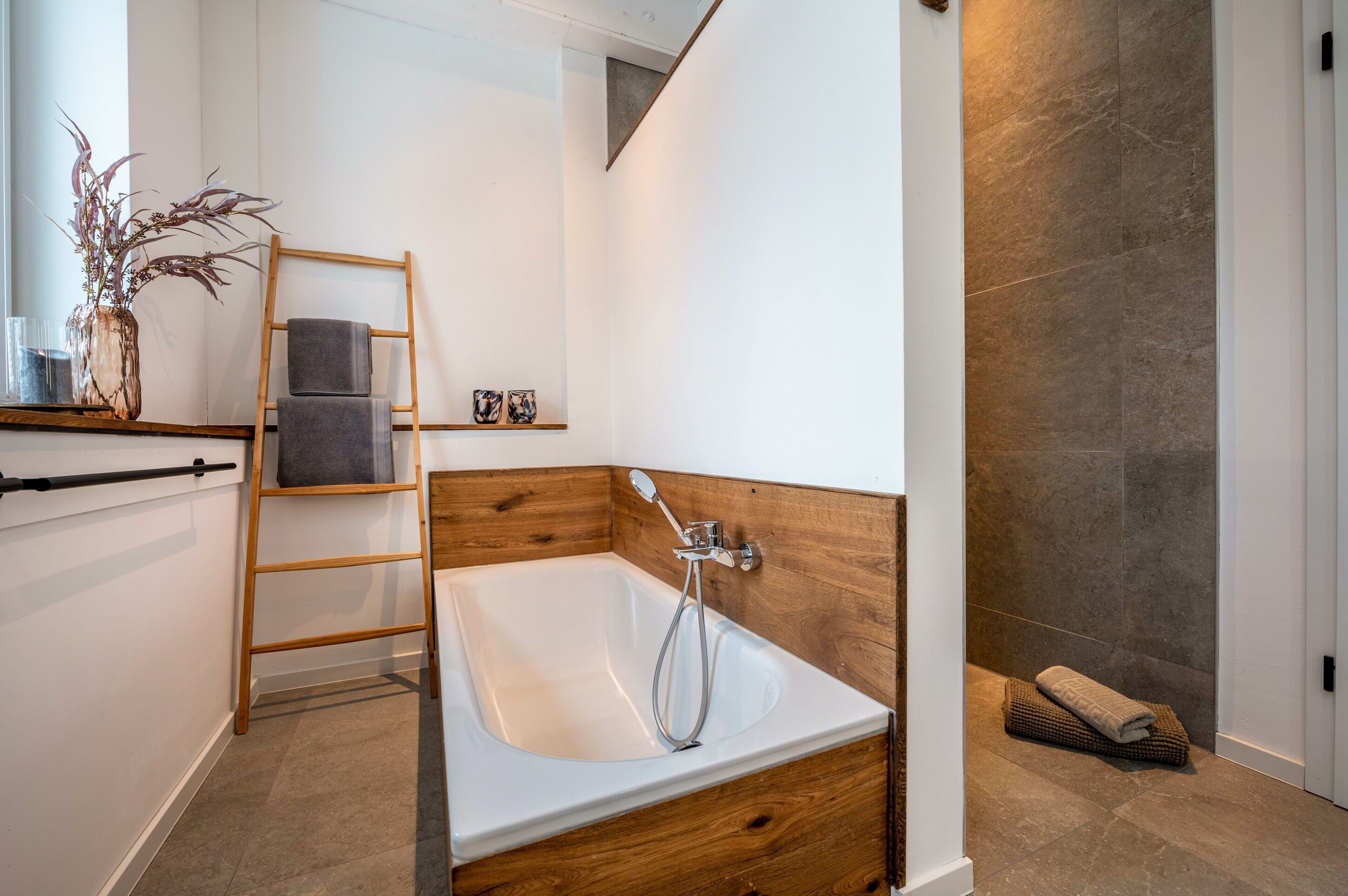A modern bathroom with a wooden vanity, a bathtub, a shower, and a wooden ladder.
