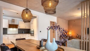 A modern kitchen with white cabinets, a wooden dining table, and hanging wicker pendant lights.