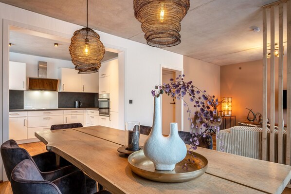 A modern kitchen with white cabinets, a wooden dining table, and hanging wicker pendant lights.
