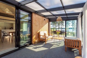 A modern outdoor patio with a wooden deck, seating area, and a view of a lake. - Villa Pickala - Design - Seafront - Hot tub (Siuntio)