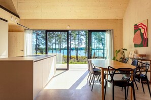 A modern kitchen with a large window overlooking a lake, a dining area with a table and chairs, and a wooden ceiling.