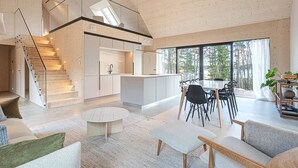 Un vaste espace de vie doté d’un haut plafond, une cuisine avec des meubles modernes, un coin repas avec une table ronde et un escalier menant à l’étage supérieur.