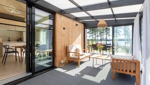 Un intérieur moderne avec un mur en verre, un mur lambrissé en bois et un coin salon offrant une vue sur un lac.