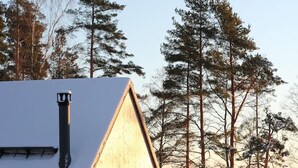 Une cabane en bois dotée d’une grande fenêtre et d’un toit en pente, entourée de neige et d’arbres.