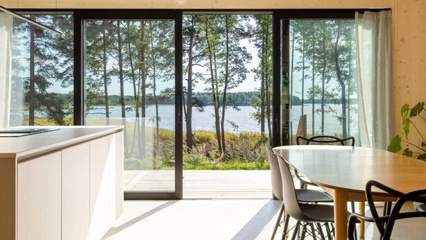 Une cuisine moderne dotée d’une grande fenêtre donnant sur un lac et une forêt.