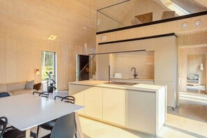 A modern kitchen with a central island, a dining area with a table and chairs, and a view of the outdoors through a large window. - Villa Pickala - Design - Seafront - Hot tub (Siuntio)