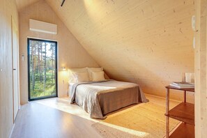 A bedroom with a sloped ceiling, a bed, a bedside table, and a window with a view of trees. - Villa Pickala - Design - Seafront - Hot tub (Siuntio)